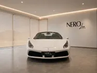 The white Ferrari 488 Spider is showcased from the front in a modern NEROline showroom in Zurich, highlighting its elegant design.