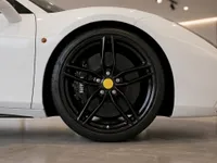 The front wheel and side profile of a white Ferrari 488 Spider with black rims and yellow center caps, available in Zurich.