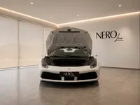 A white Ferrari 488 Spider is displayed head-on with its front hood open in a modern NeroLine showroom in Zurich.