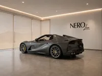 The dark grey Ferrari 812 GTS is showcased from a rear three-quarter angle in a modern showroom in Lausanne.