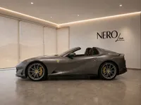 The Ferrari 812 GTS in gloss Grigio Silverstone dark grey, shown from the side with its roof down in a Lausanne showroom.