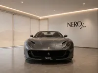 The Ferrari 812 GTS in gloss Grigio Silverstone dark grey is showcased from the front view in a modern showroom in Lausanne.
