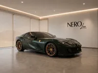 The dark green Ferrari 812 GTS with bronze wheels is elegantly displayed at a front three-quarter angle in a modern Zurich showroom.