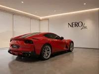 The red Ferrari 812 Superfast is showcased from a rear three-quarter angle in a modern showroom in Lausanne.