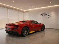 The red Ferrari F8 Spider with yellow racing stripes is parked in a modern showroom in Zurich, viewed from the rear three-quarter angle.