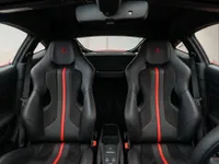 The luxurious interior of the Ferrari F8 Tributo in Lausanne, featuring black sport seats with striking red central stripes and embroidered Ferrari logos on the headrests.