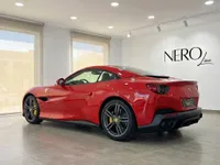 A glossy red Ferrari Portofino convertible, with its hardtop up, is parked from a rear three-quarter angle in a bright showroom in Madrid.