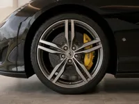 The front wheel of a black Ferrari Portofino in Zurich, featuring a silver multi-spoke rim and yellow brake caliper.