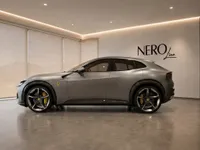 The 2023 Ferrari Purosangue in satin silver-grey is showcased in a modern showroom in Lausanne, viewed from the side.