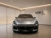 The satin silver-grey Ferrari Purosangue is prominently displayed from the front in a stylish Nero Line showroom in Lausanne.
