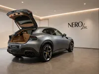 The satin silver-grey Ferrari Purosangue is showcased from a rear three-quarter angle with its trunk open in a Lausanne showroom.