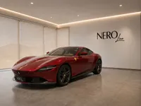 The gloss red Ferrari Roma is elegantly displayed from a front-three-quarter angle in a modern showroom in Lausanne.