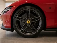 The front wheel and fender of a red Ferrari Roma are visible, showcasing the sleek design and alloy wheel in Lausanne.