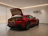 The glossy red Ferrari Roma, with its trunk open, is showcased from the rear in a modern showroom in Lausanne.