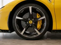 Close-up of the Ferrari SF90 Spider's front wheel, showcasing the black and silver rim, yellow brake caliper, and Giallo Modena body in Zurich.