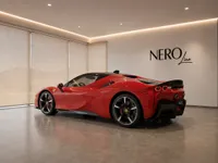 The red Ferrari SF90 Stradale is parked in a modern showroom in Lausanne, showcasing its sleek rear three-quarter profile.