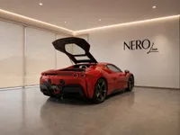 The red Ferrari SF90 Stradale is parked indoors in Lausanne, showcasing its open engine bay from a rear three-quarter view.