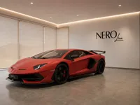 The matte red Lamborghini Aventador SVJ is elegantly displayed from a front-three-quarter view in a modern showroom in Lausanne.