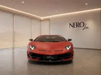 The matte red Lamborghini Aventador SVJ is prominently displayed in a showroom in Lausanne, showing its striking front design.
