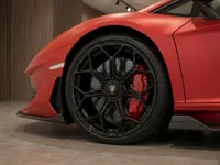 The matte red Lamborghini Aventador SVJ's front wheel, black multi-spoke rim, and red brake caliper are prominently displayed in Lausanne.