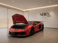 The matte red Lamborghini Aventador SVJ is displayed in a showroom in Lausanne with its front trunk open, revealing storage space.