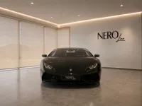A sleek gloss black Lamborghini Huracán Coupé is parked front-on in a modern NEROline showroom in Zurich.