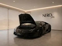 The gloss black Lamborghini Huracán Coupé is showcased with its front trunk open in a modern Zurich showroom.