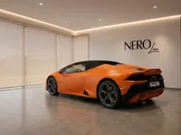 A matte orange Lamborghini Huracán EVO Spyder, seen from the rear three-quarter angle, parked in a modern NEROline showroom in Zurich.