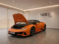 Matte orange Lamborghini Huracán EVO Spyder with its front hood open, displayed in a modern NEROline showroom in Zurich.