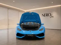 A bright blue Lamborghini Huracán Spyder with its front hood open, parked in a modern showroom in Zurich.