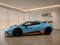 A light blue and orange Lamborghini Huracán STO is parked in a modern showroom in Lausanne, showcasing its sleek side profile.