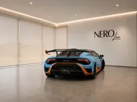 The rear view of a light blue and orange Lamborghini Huracán STO, parked in a modern showroom in Lausanne.
