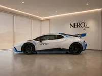 White Lamborghini Huracán STO with blue accents, parked indoors in a modern showroom in Zurich.