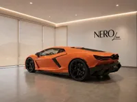 The orange Lamborghini Revuelto is parked in a modern showroom, showcasing its sleek rear three-quarter profile in Lausanne.