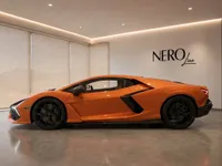 The orange 2024 Lamborghini Revuelto supercar is showcased from its side profile in a modern showroom in Lausanne.
