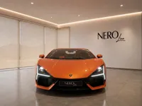 The 2024 Lamborghini Revuelto in gloss orange is prominently displayed from a front view in a showroom in Lausanne.