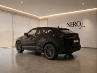 The gloss black Lamborghini Urus is showcased from a rear three-quarter angle in a modern, well-lit showroom in Lausanne.