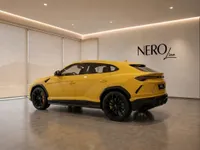 The 2021 Gloss Yellow Lamborghini Urus is showcased from a rear three-quarter angle in a modern indoor setting in Lausanne.
