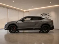 The grey 2019 Lamborghini Urus is shown in a side profile view, parked indoors in a modern showroom in Zurich.