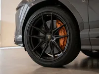 The front wheel of a grey Lamborghini Urus is visible, showcasing its black multi-spoke rim and vibrant orange brake caliper in Zurich.