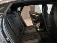 The luxurious rear interior of the Lamborghini Urus in Zurich, featuring black leather seats with orange hexagonal stitching and an open door.
