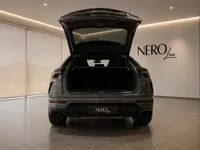 The rear view of a grey Lamborghini Urus with its trunk open, parked in a modern showroom in Zurich.
