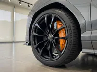 A close-up view of the grey Lamborghini Urus's front wheel, featuring a black multi-spoke rim and vibrant orange brake caliper in Zurich.