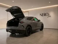 The grey 2021 Lamborghini Urus is shown from the rear three-quarter angle with its trunk open in a showroom in Zurich.