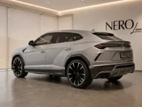 The silver Lamborghini Urus is showcased from a rear three-quarter view, parked in a modern showroom in Zurich with the NERO Line logo.