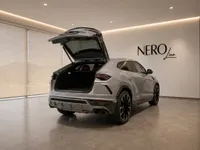 The silver Lamborghini Urus is seen from the rear with its trunk open, parked in a sleek, modern showroom in Zurich.