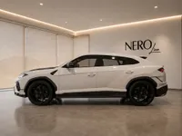 The white 2023 Lamborghini Urus Performante is showcased in a luxurious showroom, viewed from its elegant side profile in Zurich.