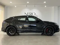 The Gloss Black Lamborghini Urus SE is parked in a showroom, showcasing its sleek side profile and black wheels with red brake calipers in Barcelona.