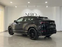A glossy black Lamborghini Urus SE is parked at a rear three-quarter angle in a showroom in Barcelona.