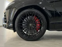 The front wheel of a black Lamborghini Urus SE in Barcelona, featuring a sleek black multi-spoke rim and vibrant red brake caliper.